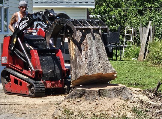 A man is standing next to a machine that is moving a large tree stump.