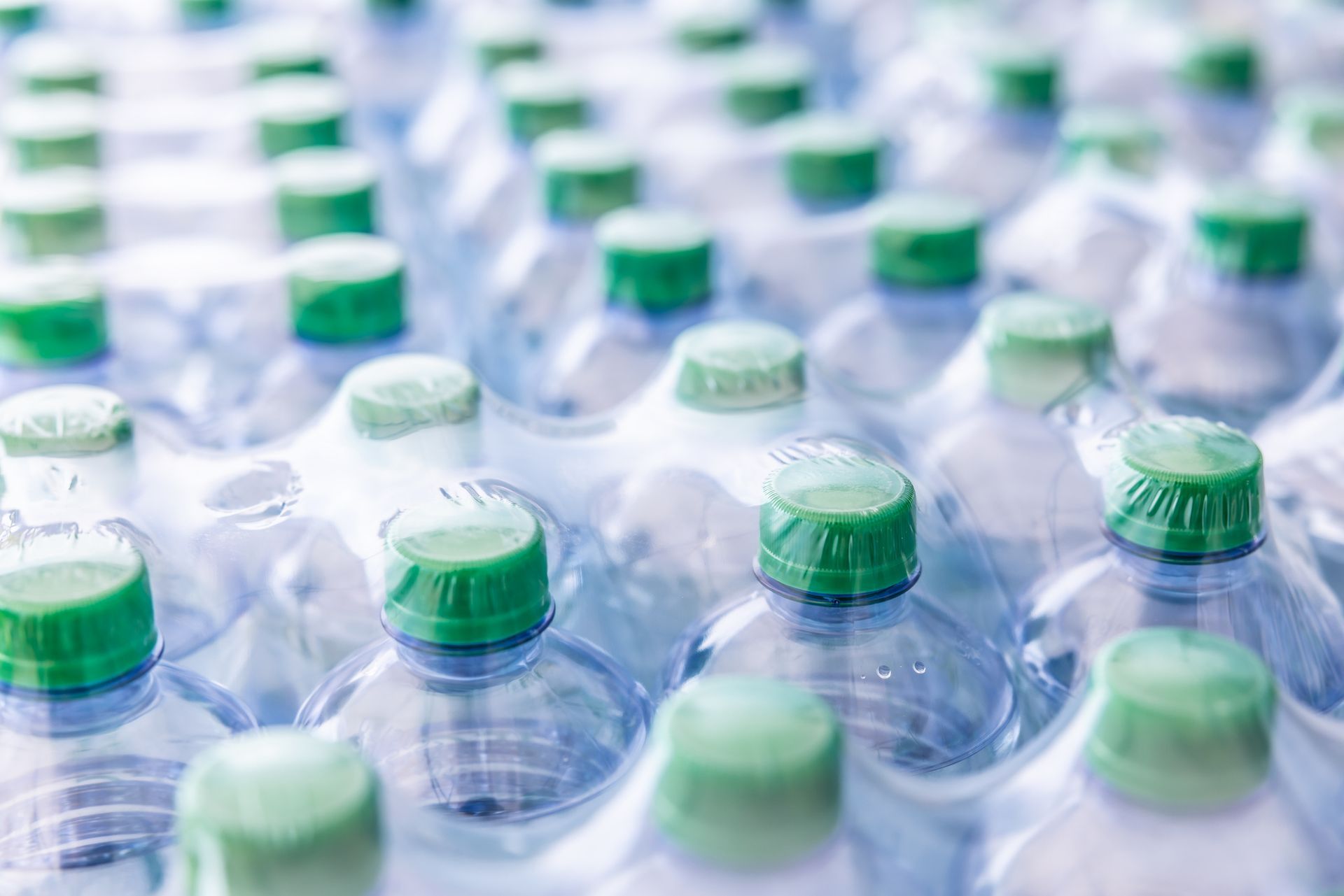A bunch of plastic water bottles with green caps stacked on top of each other.