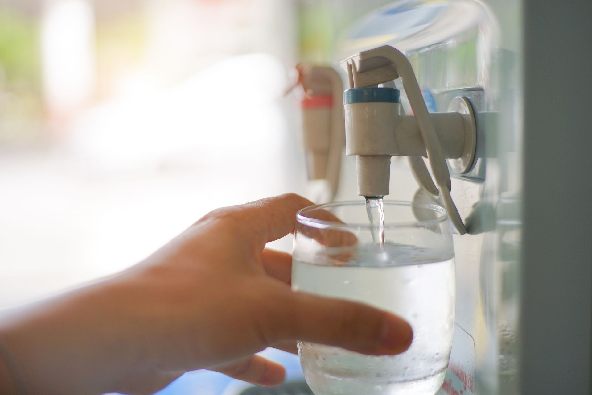 A person is pouring water into a glass from a water dispenser.