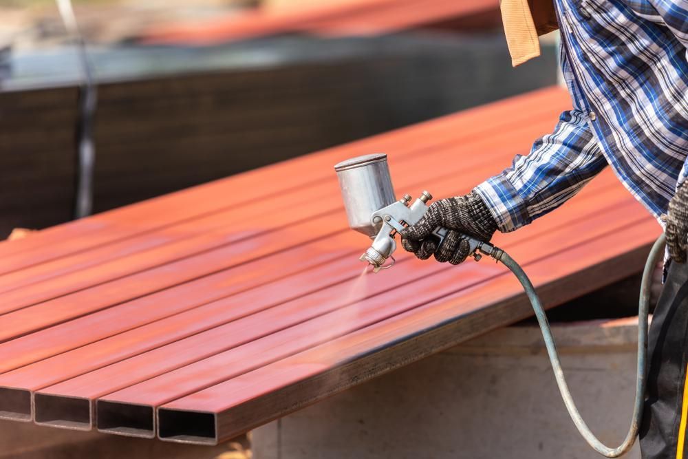 A Man Spraying A Red Paint In Piece Of Metal — Paint & Trade Supplies Lismore In Ballina, NSW