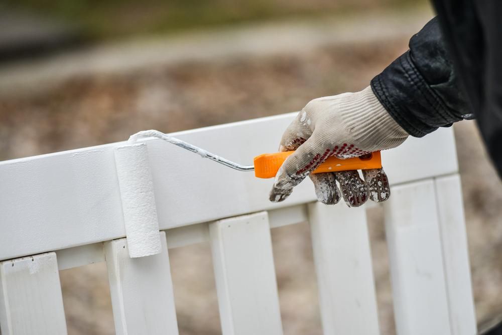 A Person Is Painting A White Fence With A Roller — Paint & Trade Supplies Lismore In Mullumbimby, NSW