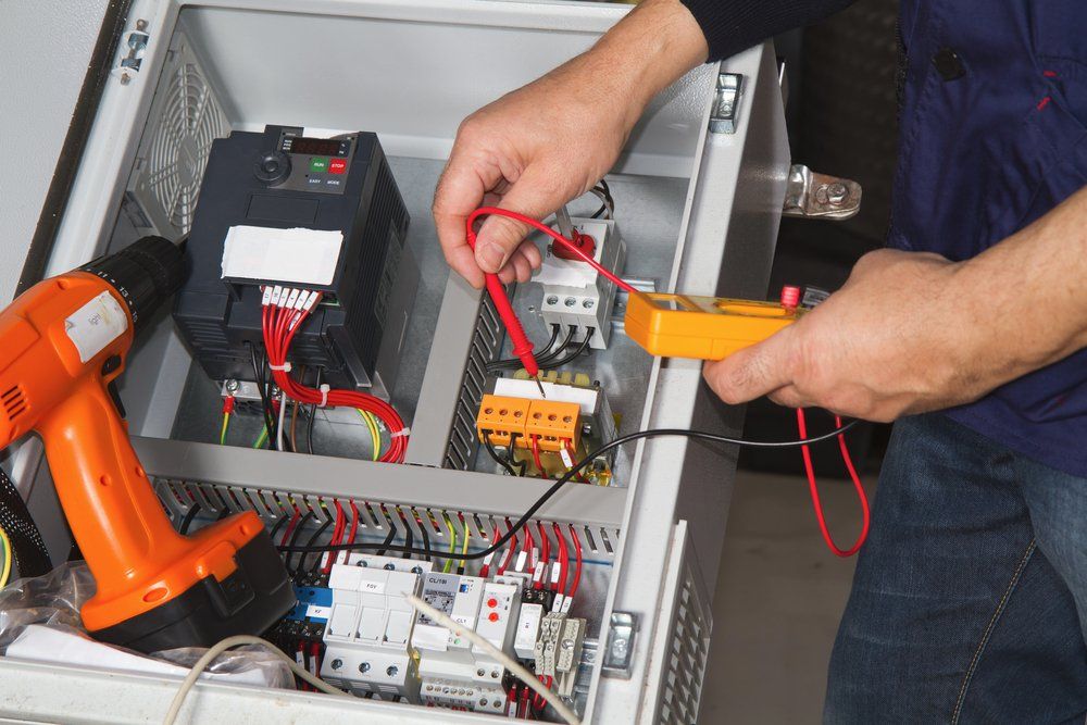 A Man is Working on an Electrical Box With a Drill and a Multimeter — Hennig Electrical Services in Maroochydore, QLD