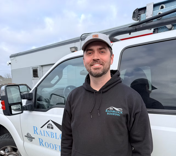 Man in a black hoodie and cap standing by a white Rainblow Roofing truck outdoors