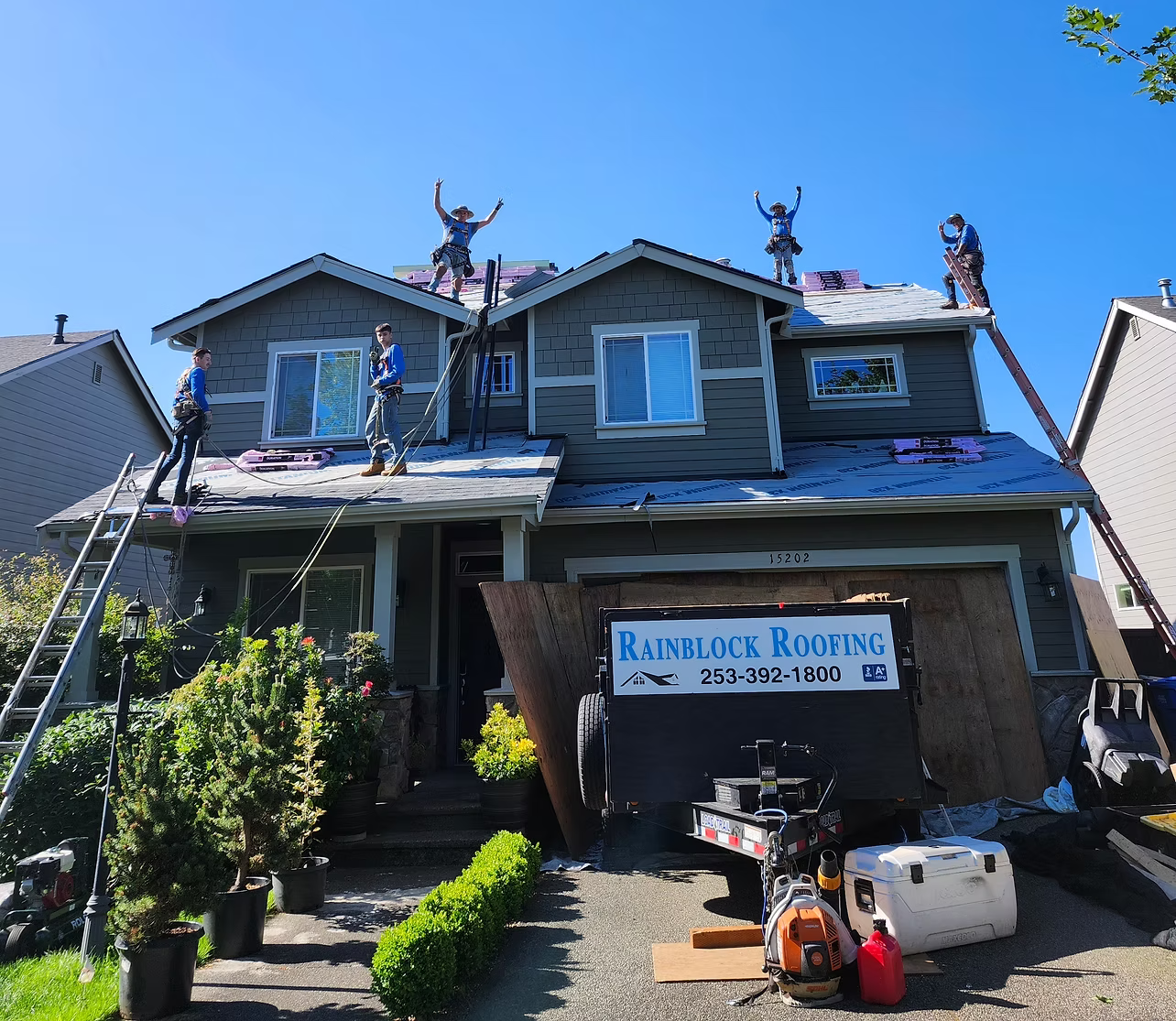 Damaged house with exposed roof; roofers work above a garage labeled “Rainbow Roofing.”