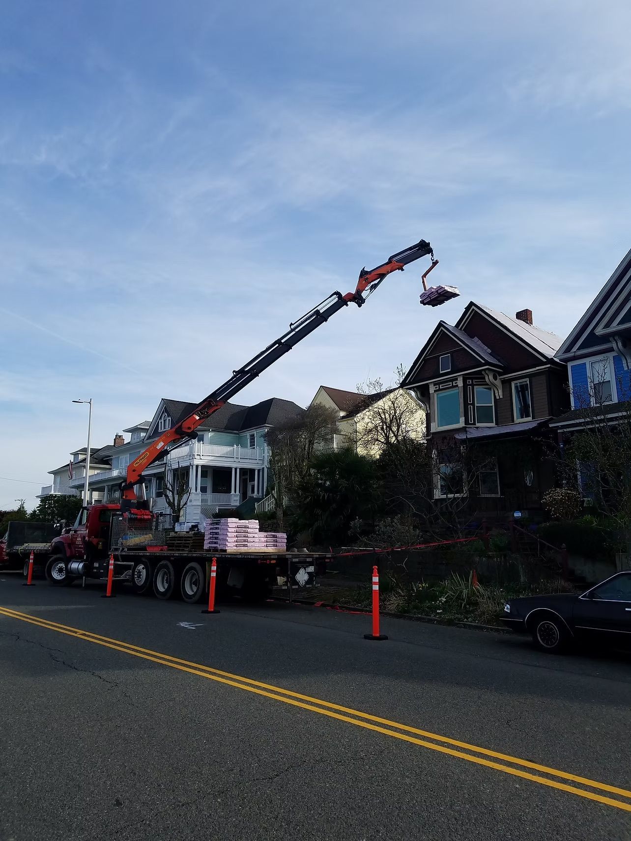 Tow truck with crane lifting debris beside damaged houses on a residential street