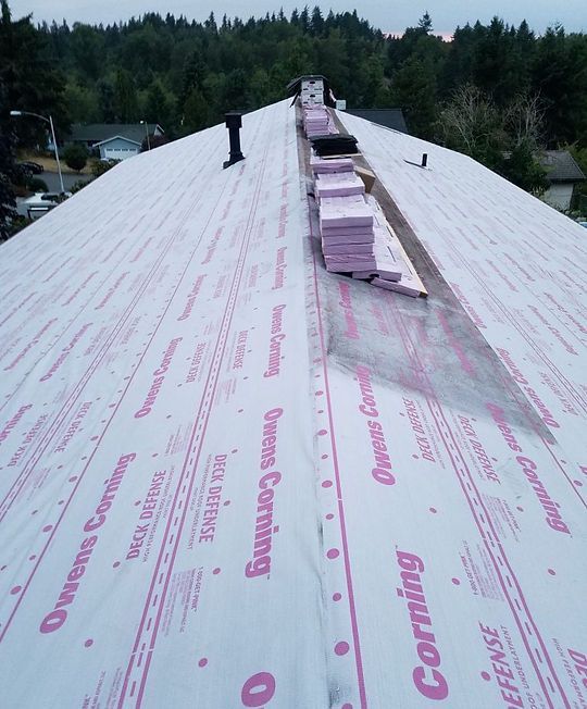 Partially installed white roofing underlayment on a steep roof with forest in the background