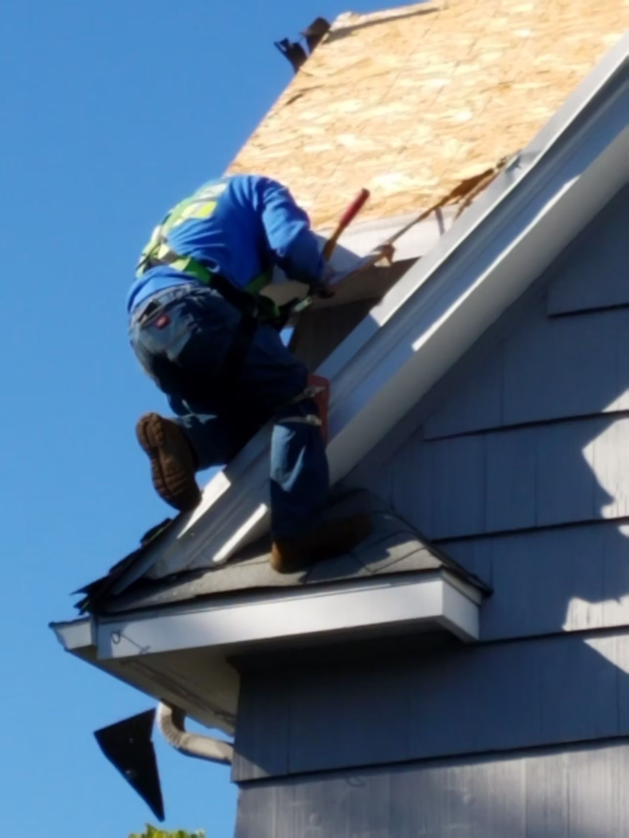 Worker on a roof repairing shingles with a hammer near a dormer window