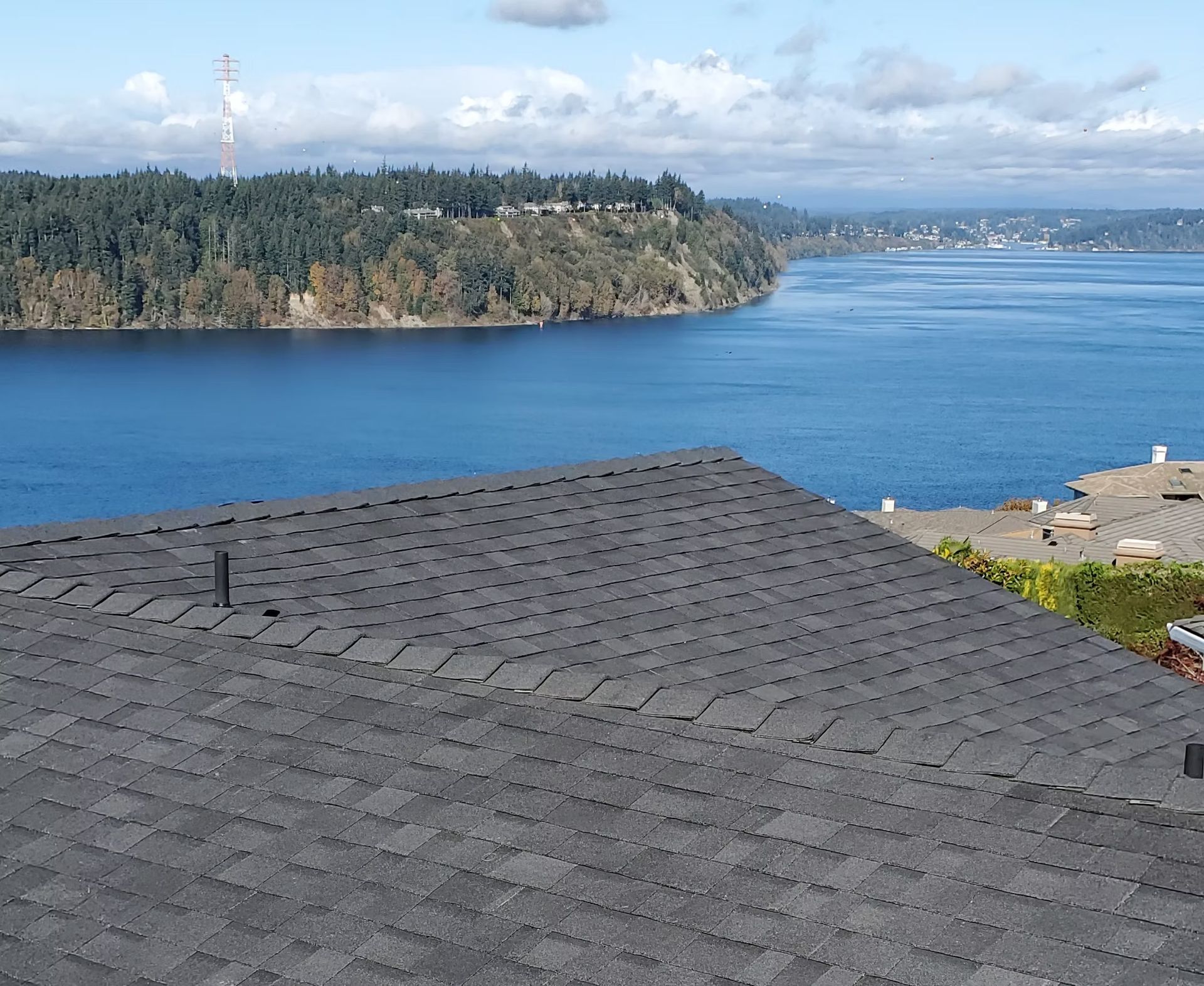 Slate roof overlooking a calm blue bay with wooded shoreline and distant city across the water