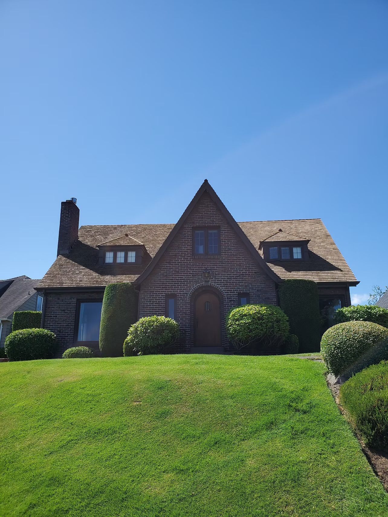 Dark shingled house with steep roof on a bright green lawn under a clear blue sky