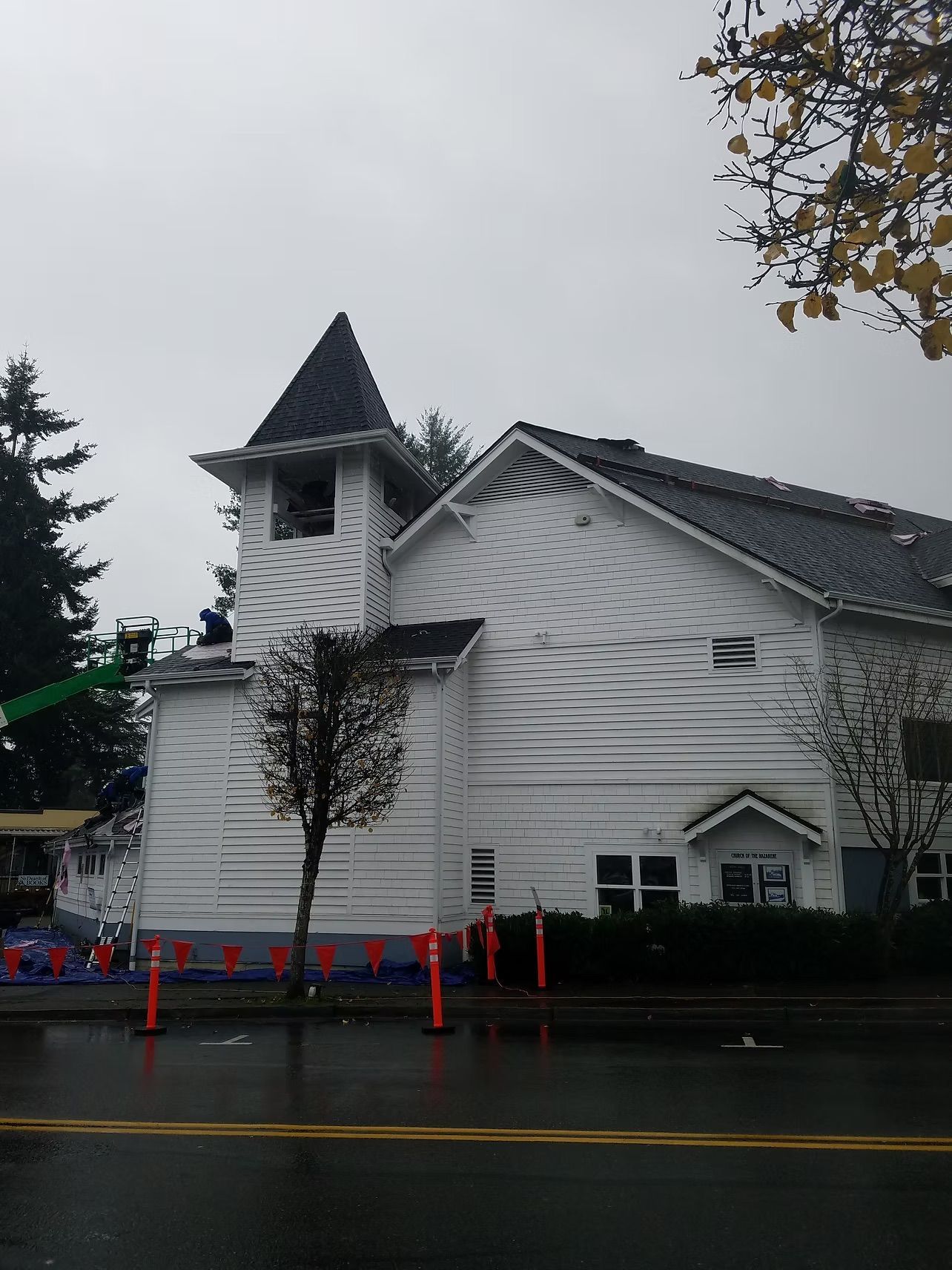 White church with steeple on a rainy street, with orange cones and trees nearby