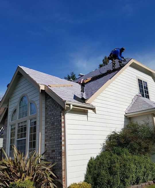 Worker on a house roof repairing shingles under a blue sky
