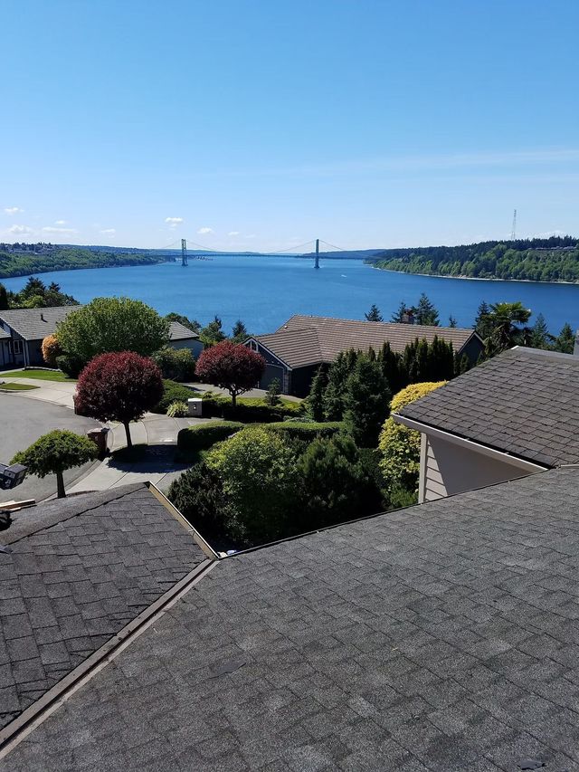 Scenic waterfront view with rooftops, manicured shrubs, and a bridge under a clear blue sky