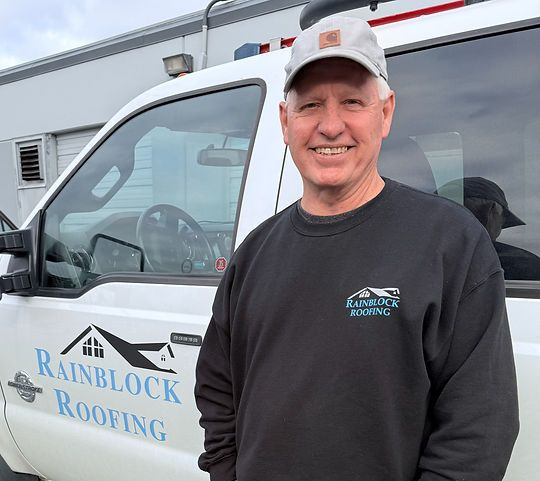 Man in a black hoodie and cap standing by a white Rainblow Roofing truck outdoors