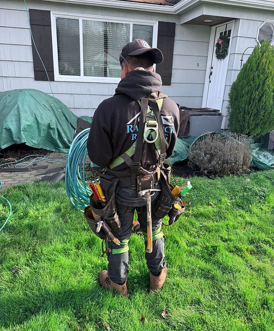 Person in climbing harness and gear standing on a lawn in front of a house.