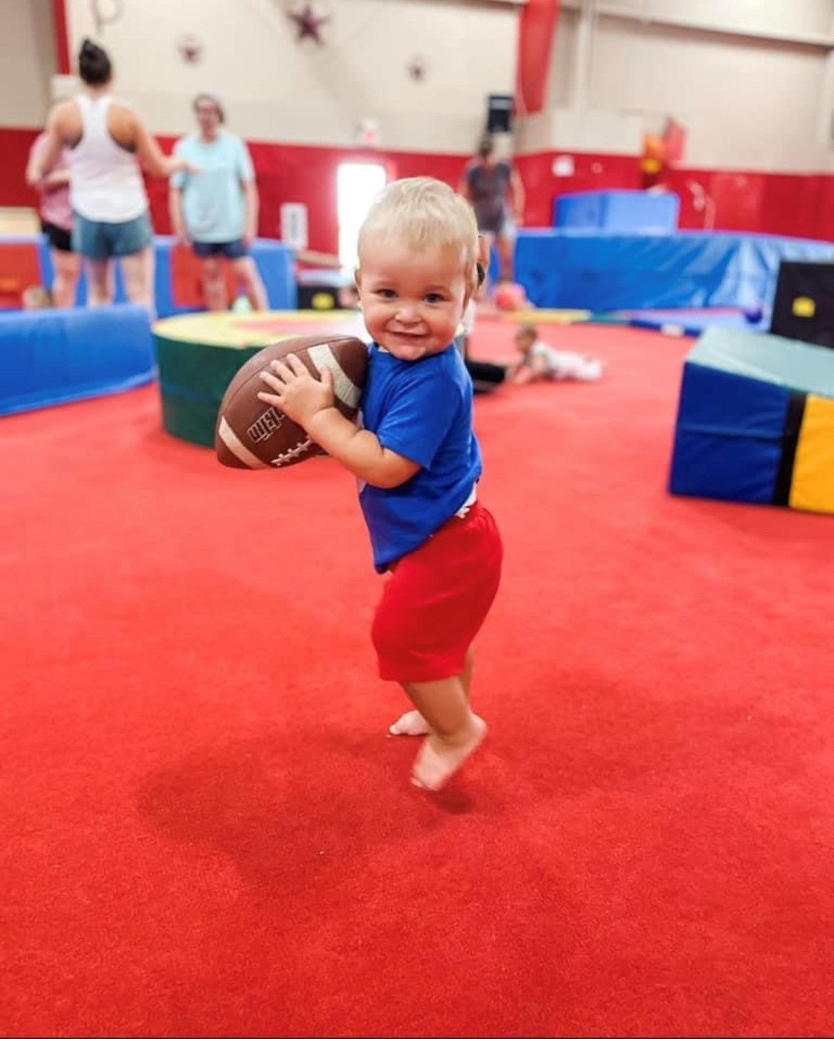 A little boy is holding a football in a gym