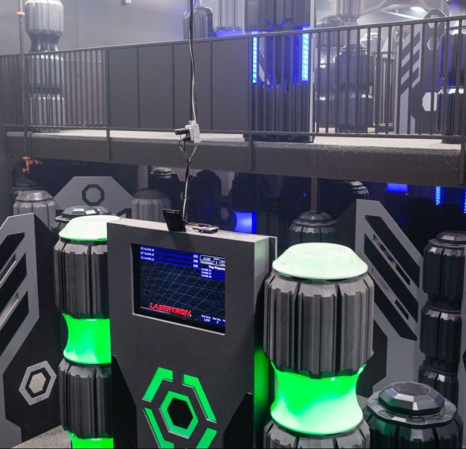 A futuristic laser tag arena with green and gray decor, a central control panel, and a raised platform.