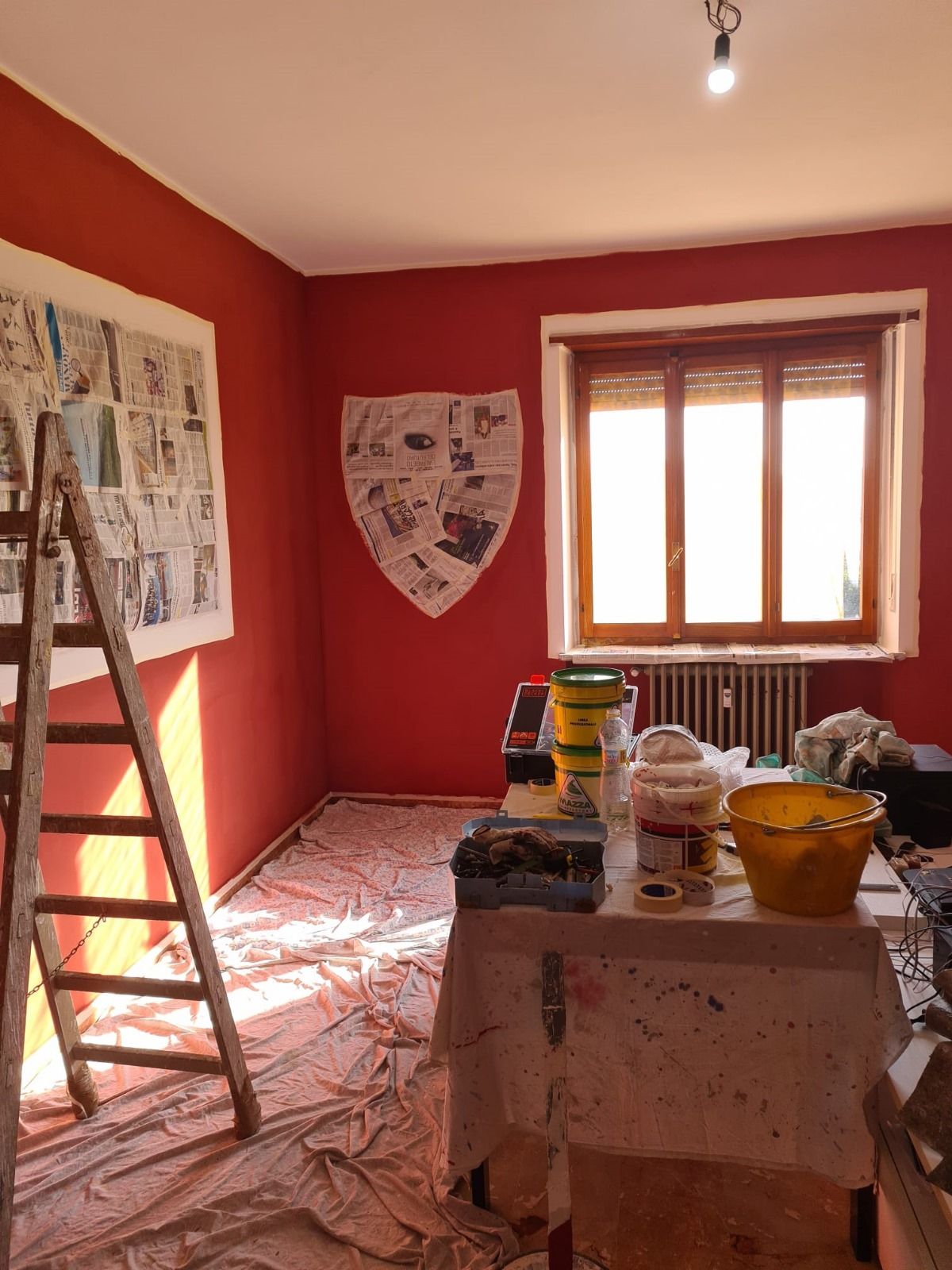 Una stanza con le pareti rosse e un tavolo con sopra dei secchi di vernice.