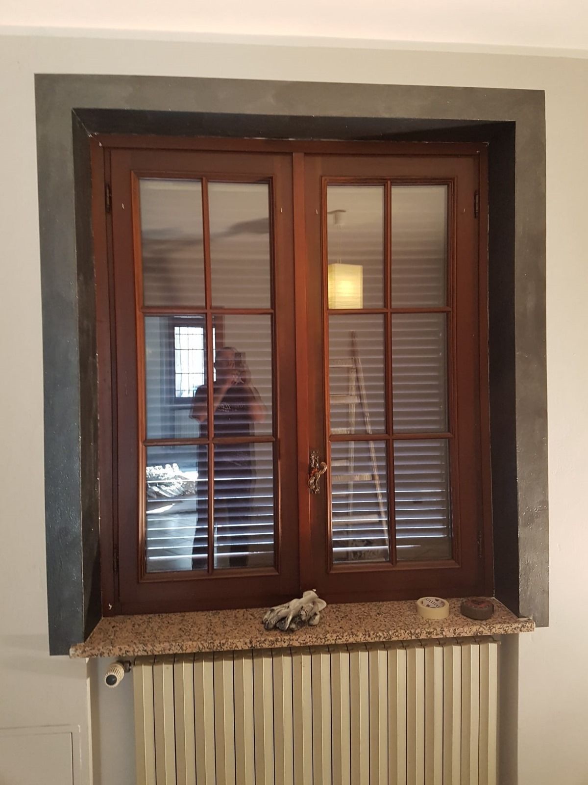 Una finestra di legno con persiane si trova in una stanza accanto a un termosifone.