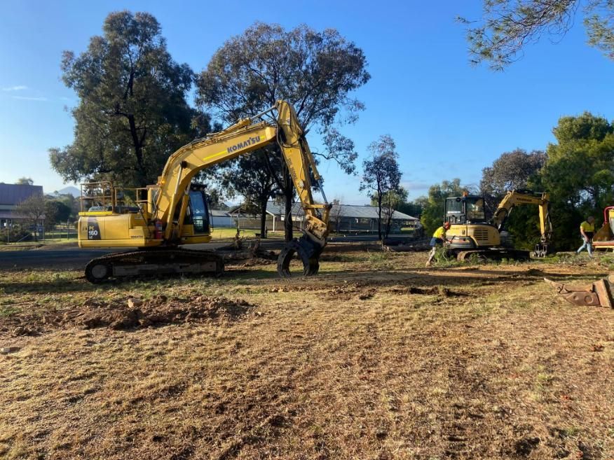 A Yellow Excavator is Driving Through a Dirt Field — Mudgee Tree Services in Eurunderee, NSW