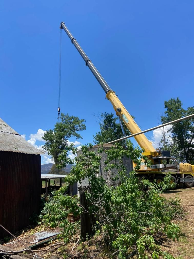 A Large Yellow Crane Is Lifting a Tree in Front of A Barn — Mudgee Tree Services in Eurunderee, NSW