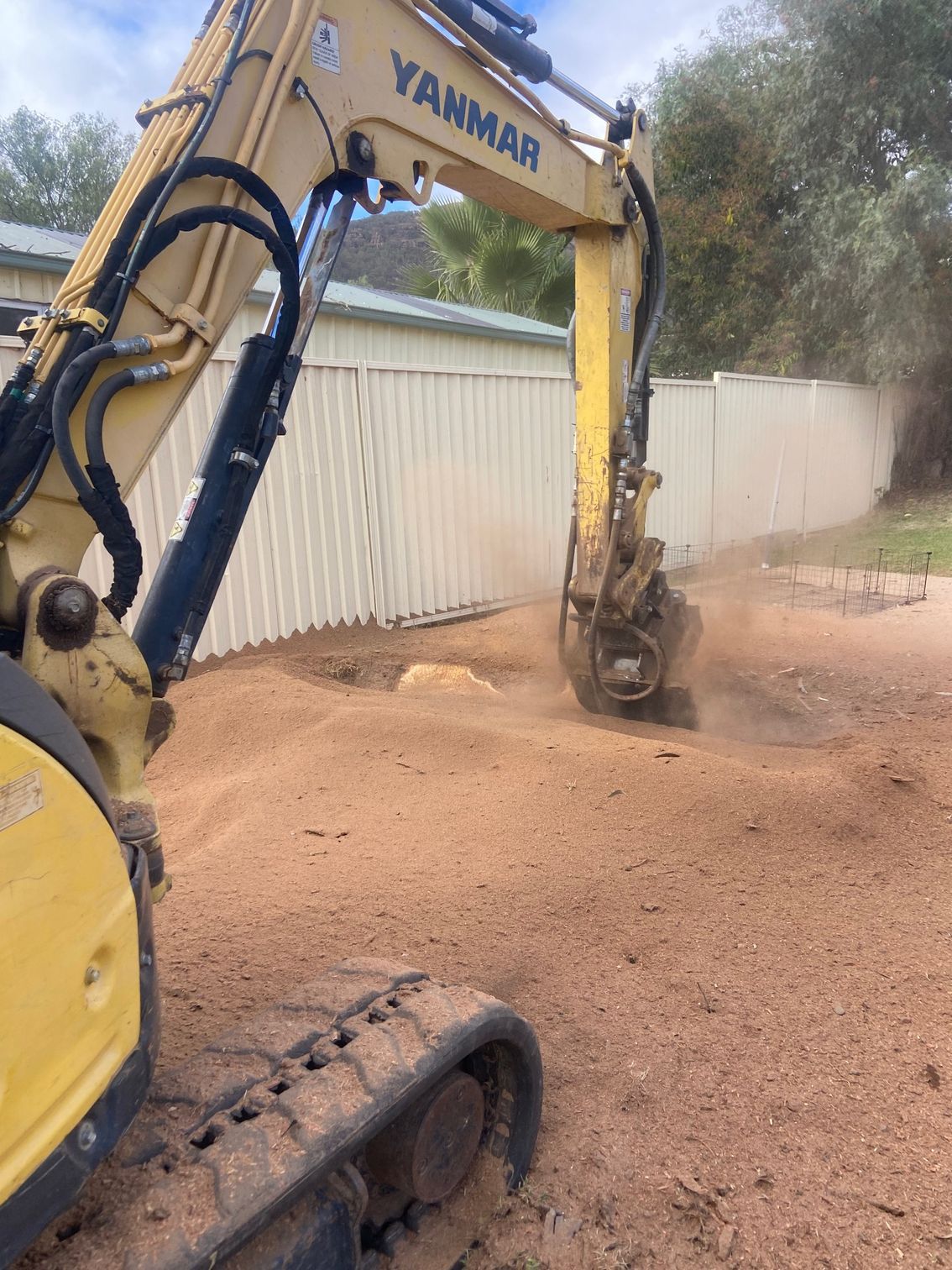 A Yellow digger is digging out a hole in a backyard— Mudgee Tree Services in Eurunderee, NSW