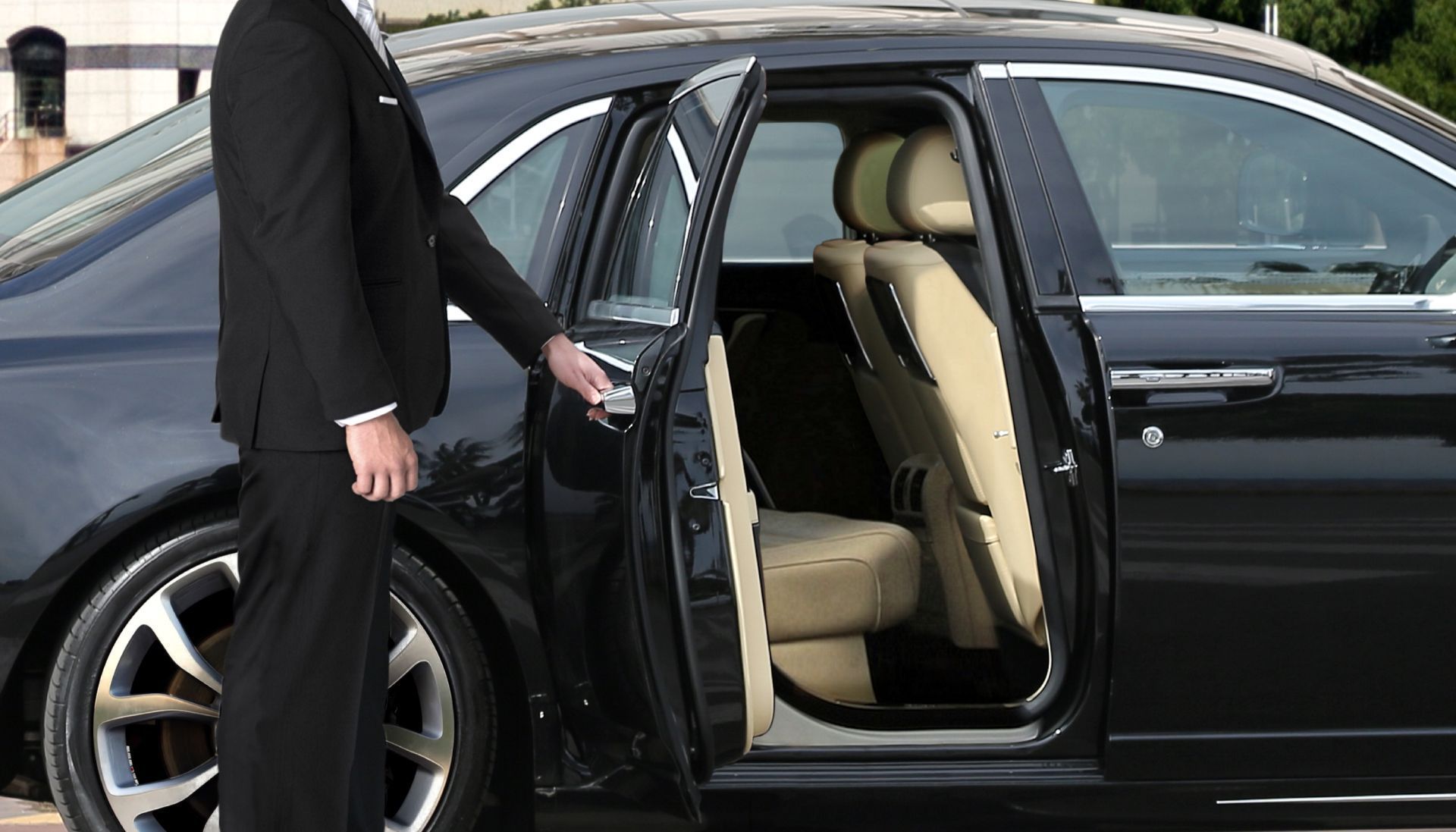 Man in suit opening a black car door for a passenger.