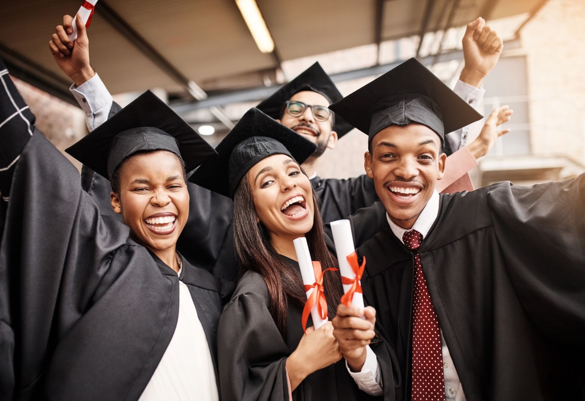 Graduates in black caps and gowns with diplomas, smiling and celebrating outdoors.