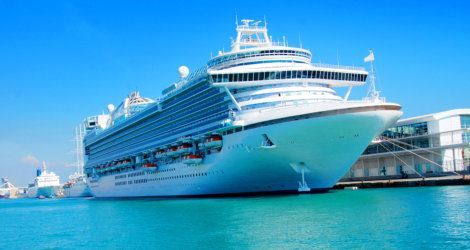 Cruise ship docked at harbor with blue water and sky.