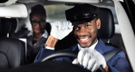 Smiling chauffeur in uniform, behind the wheel, looking at the camera. Passenger in the back.