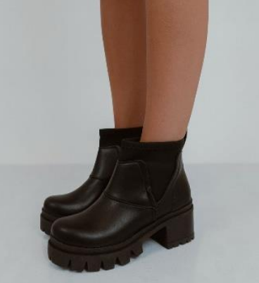 Botines negros con suela gruesa con tacos en las piernas de una persona.