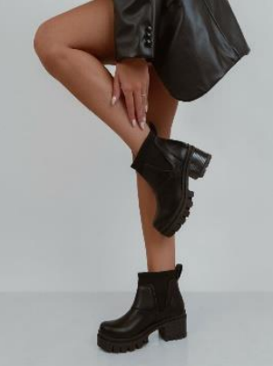 Botines negros con suela gruesa con tacos en las piernas de una persona.