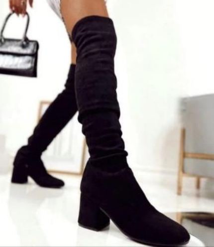 Mujer que lleva botas negras por encima de la rodilla con tacón de bloque y sosteniendo un bolso.
