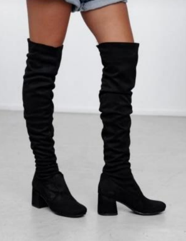 Mujer que lleva botas negras por encima de la rodilla con tacones de bloque y caña fruncida.