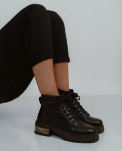 Persona con pantalones y botas negras. Un pie está inclinado hacia arriba. Las botas tienen suela gruesa.