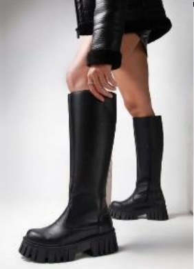 Persona que lleva botas altas de plataforma negras, en un entorno interior.