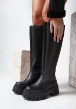 Persona que lleva botas altas de plataforma negras, en un entorno interior.