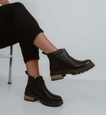 Mujer con botas negras con tachuelas, sentada, con las piernas cruzadas.