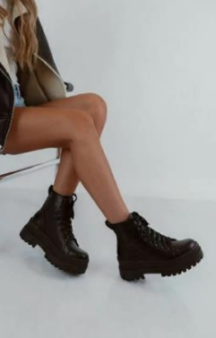 Mujer que lleva botas de combate con cordones de color marrón oscuro, sentada con las piernas cruzadas.