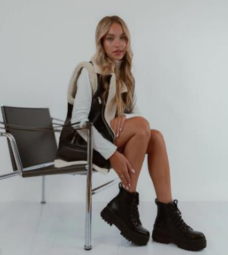 Mujer que lleva botas de combate con cordones de color marrón oscuro, sentada con las piernas cruzadas.