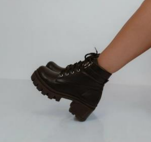 Botines de piel de color negro con suela gruesa en la caña, en ángulo frente a un fondo blanco.