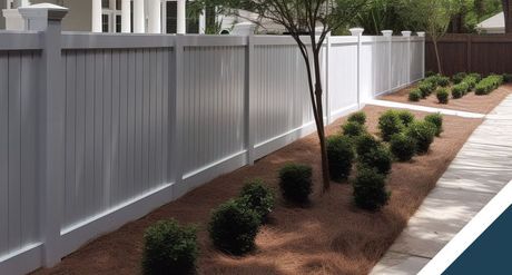 A white fence surrounds a yard with bushes and trees.
