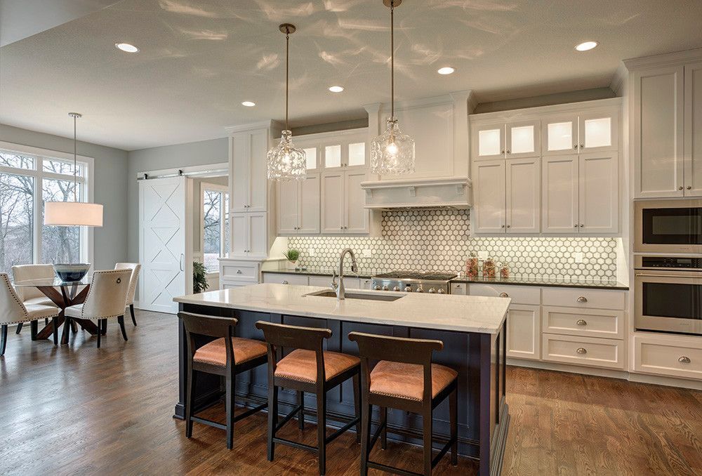 A kitchen with white cabinets , a large island , stools and a dining room