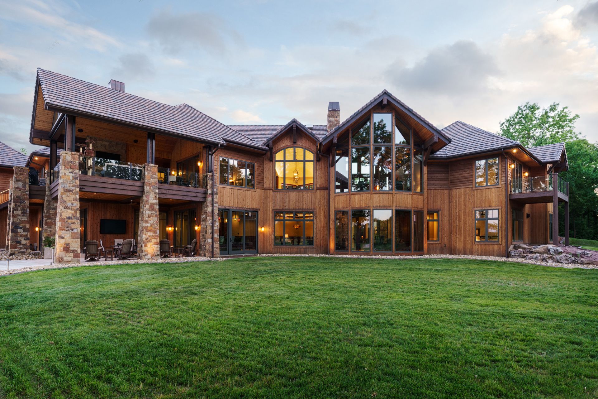 A large wooden house with a lot of windows is sitting on top of a lush green field