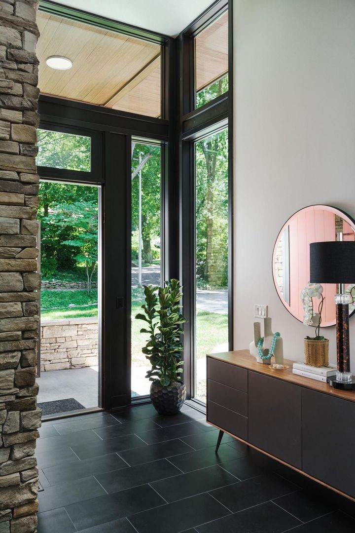 A hallway with a dresser , mirror , and large windows.