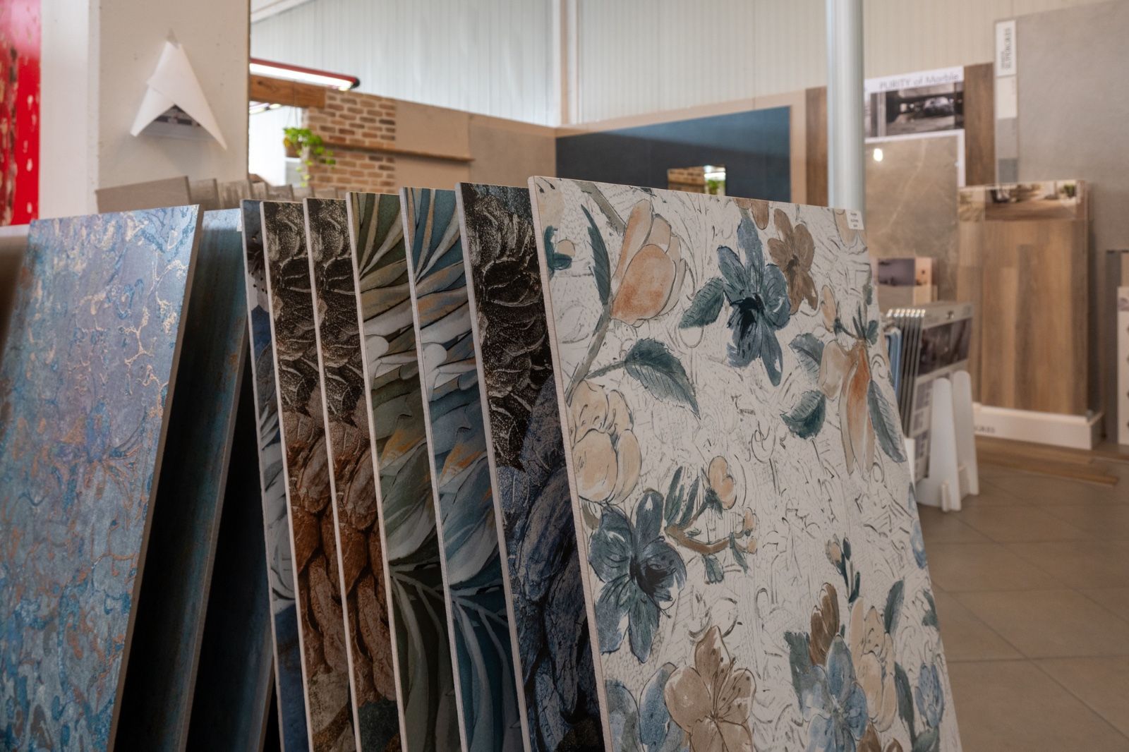 Campioni di piastrelle esposti in uno showroom, con motivi floreali e testurizzati in vari colori.