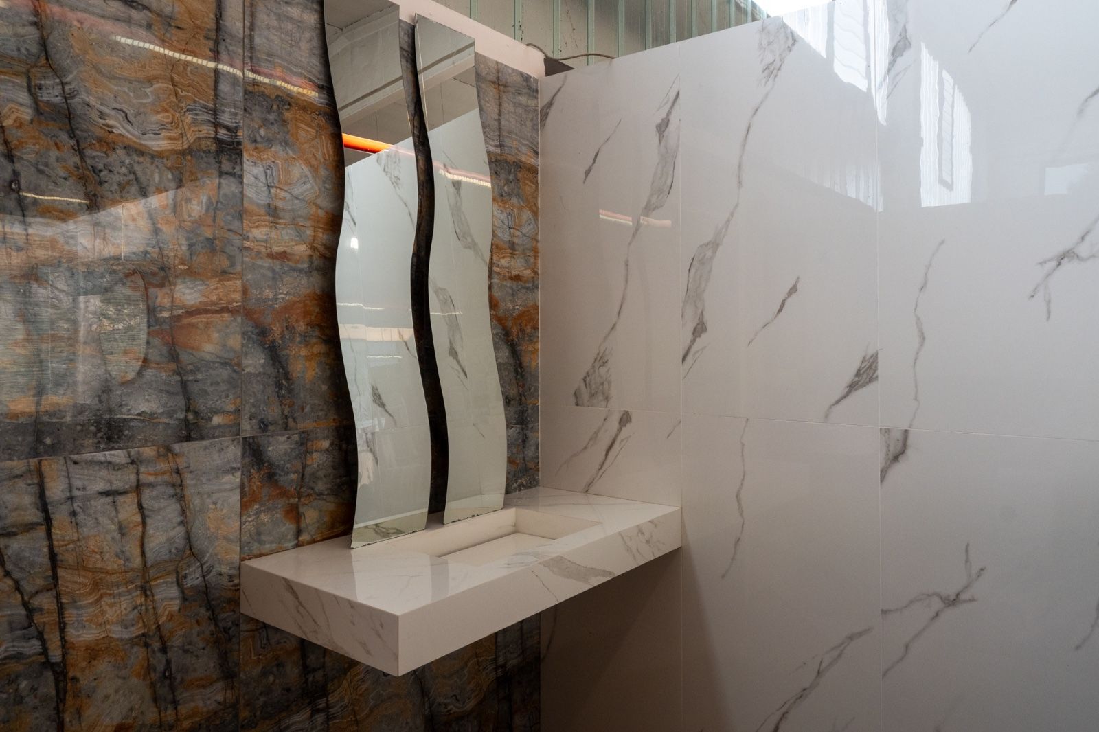 Un bagno moderno con mobiletto e parete in marmo bianco, uno specchio dalla forma particolare e una parete in pietra.