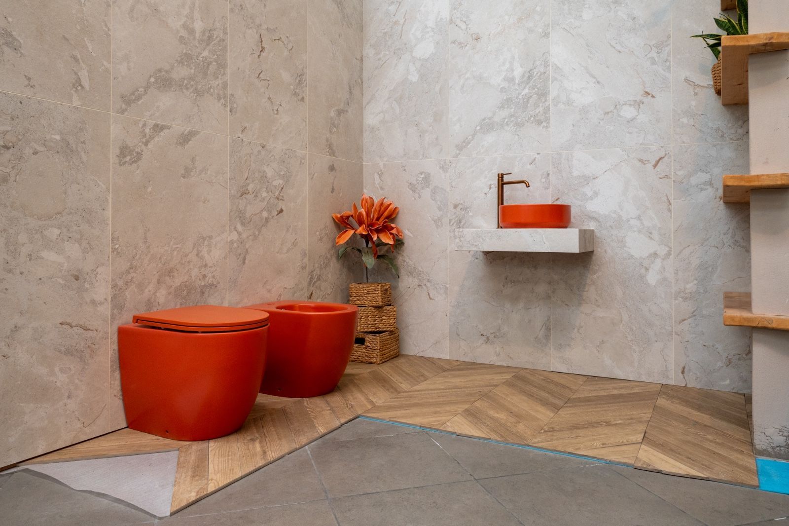 Bagno moderno con dettagli arancioni: lavandini, sgabelli. Pareti in marmo marrone chiaro, pavimento in legno.