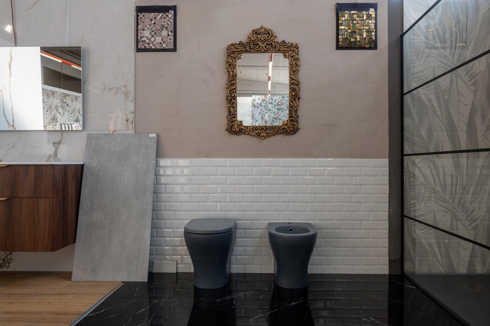 Esposizione del bagno con sanitari grigi, piastrelle bianche della metropolitana e specchio dorato decorato.