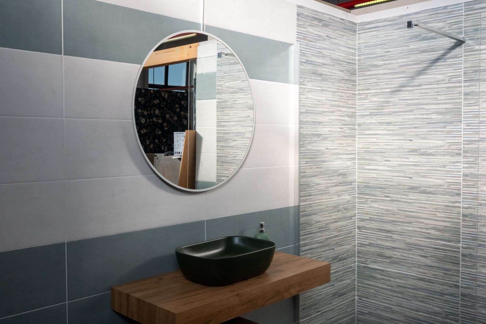 Bagno con specchio ovale, mensola in legno, lavandino scuro e piastrelle grigie e blu.