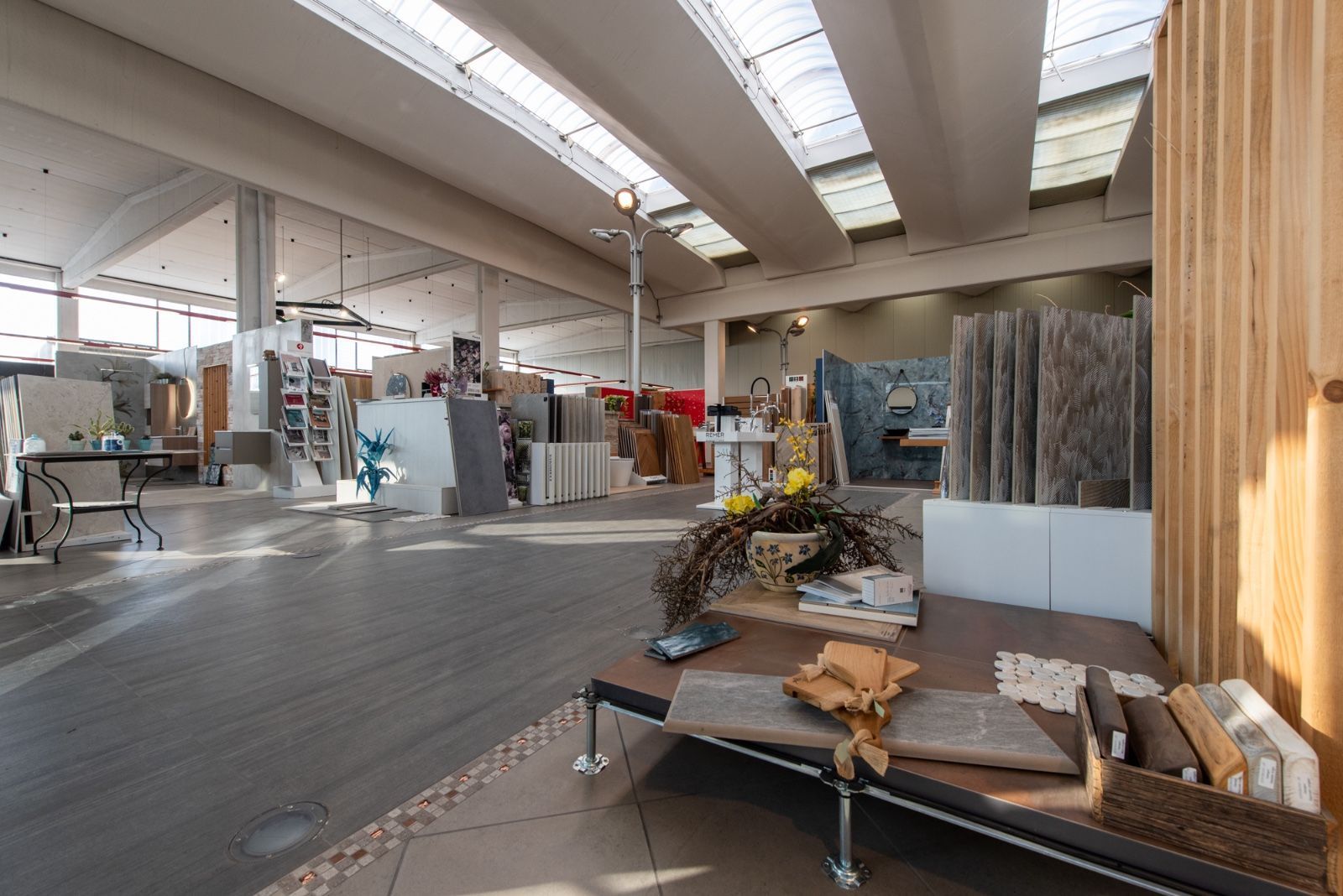 Ampio showroom con vari campioni di pietre e piastrelle. La luce naturale proveniente dai lucernari illumina lo spazio.